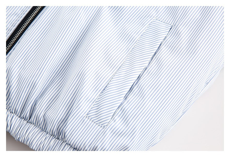 Close-up of a white garment with narrow blue stripes, a black zipper, a slit pocket, and a gathered edge.
