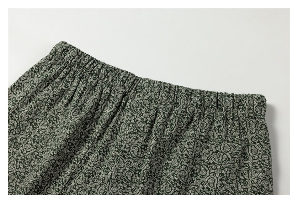 Flat close-up of the gathered waistband and upper section of dark green paisley-print bottoms.