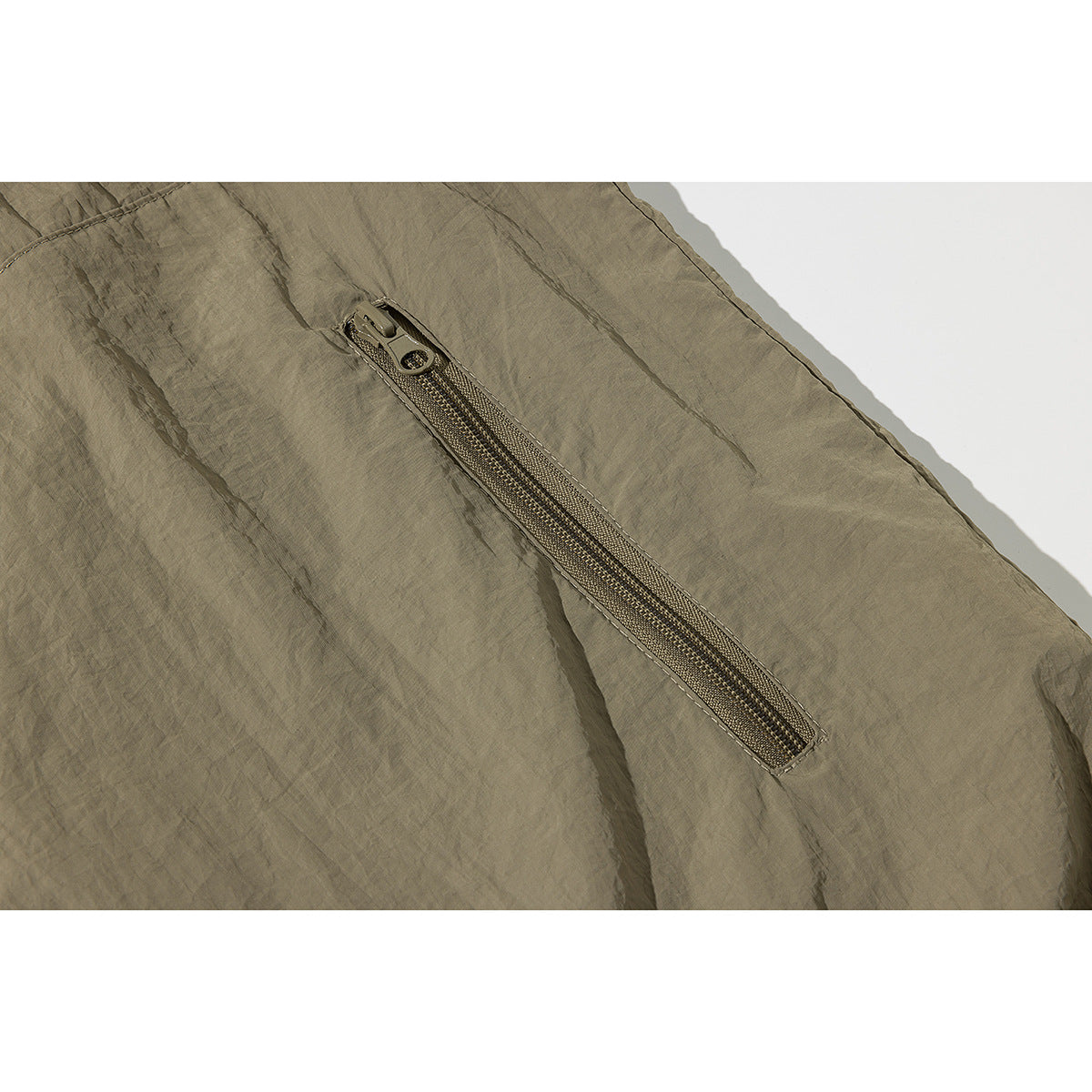 Close-up of a long diagonal zipper pocket on wrinkled olive-taupe fabric.