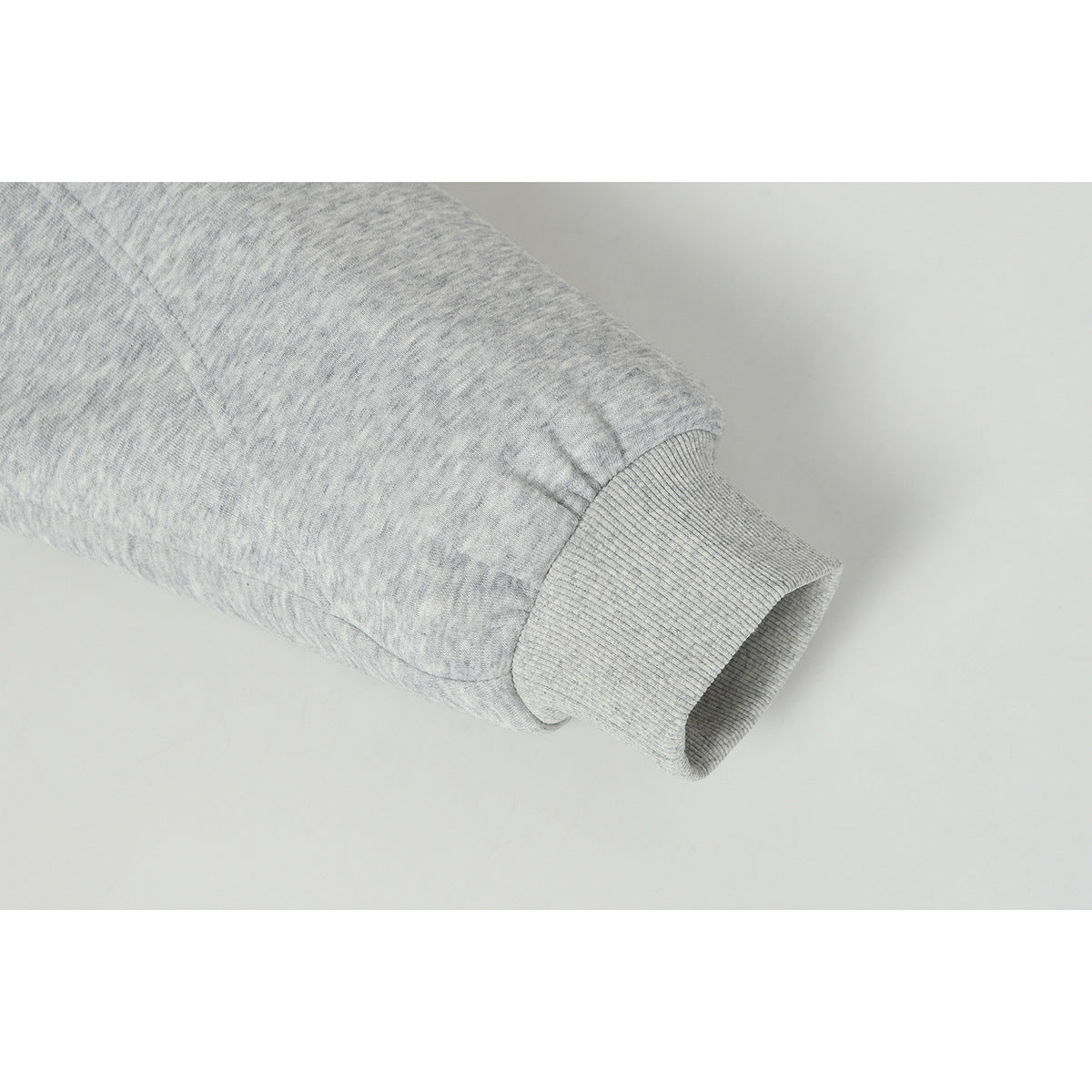 Close-up of a light gray melange jacket sleeve ending in a ribbed cuff.