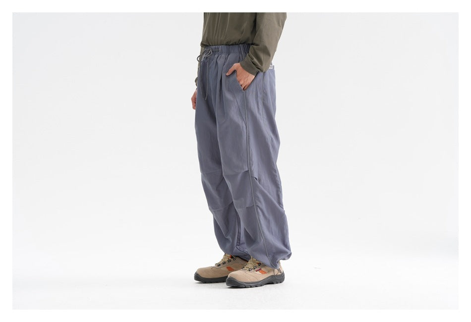 Three-quarter side view of a model wearing loose slate-blue drawstring trousers with a side pocket.