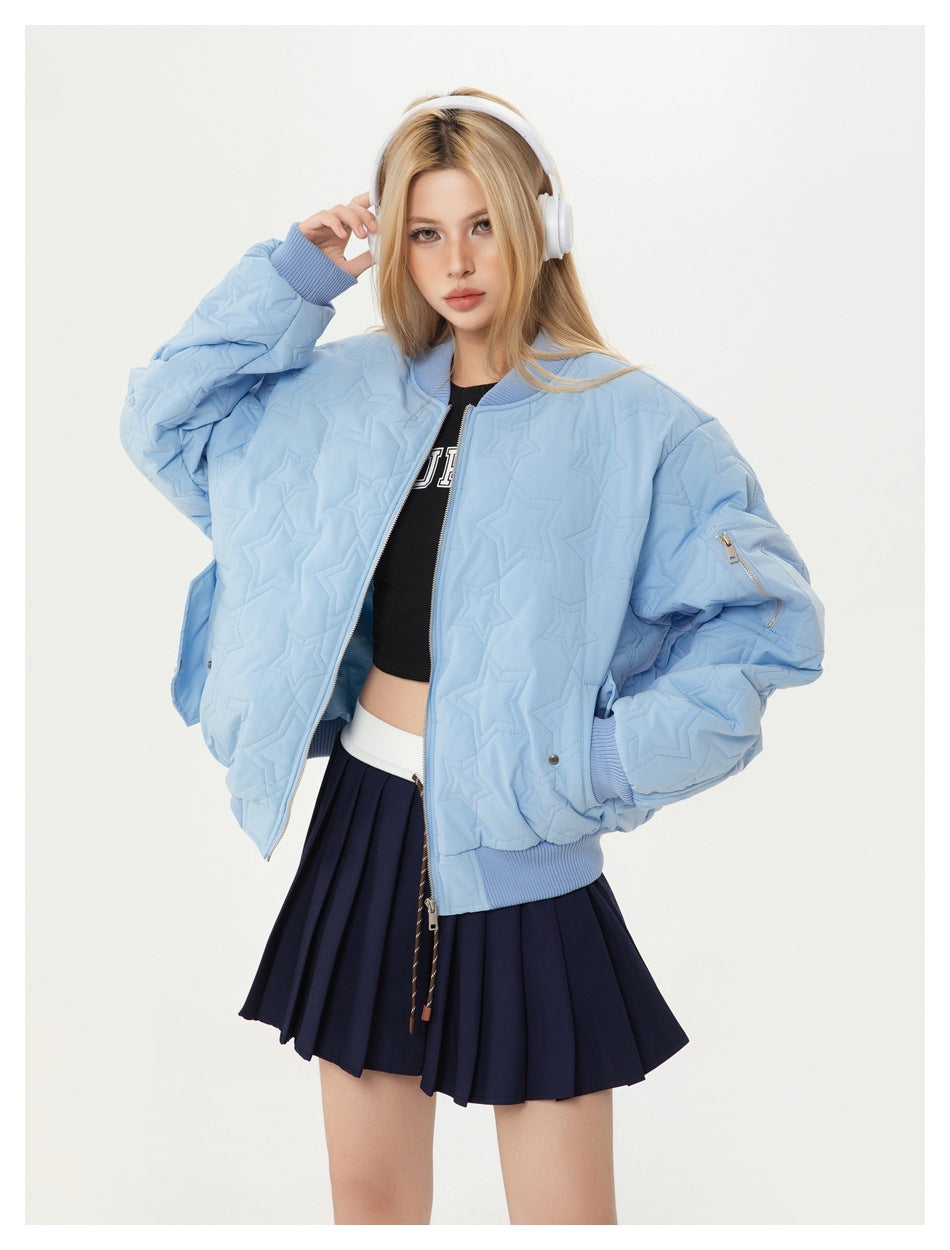 Model wearing an open light blue star-quilted bomber jacket with ribbed trim and a navy pleated skirt.
