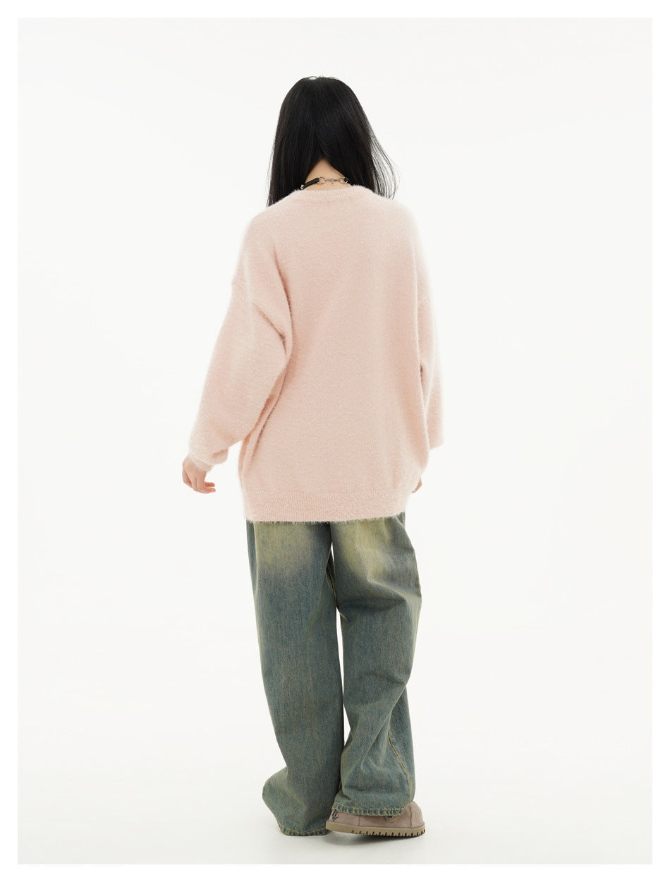 Back view of a model wearing a plain pale pink oversized sweater with ribbed cuffs and hem and loose jeans.