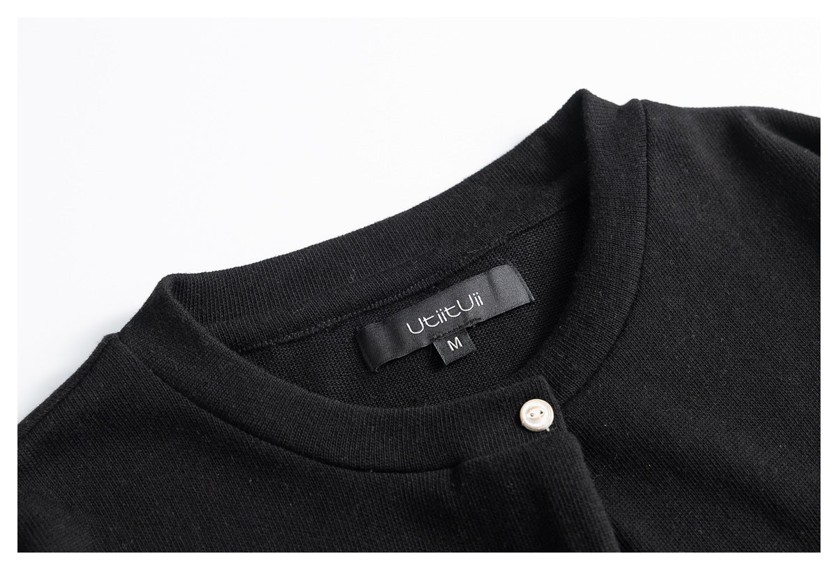 Close-up of a black knit garment's round neckline, sewn-in size M label, and small pale button.