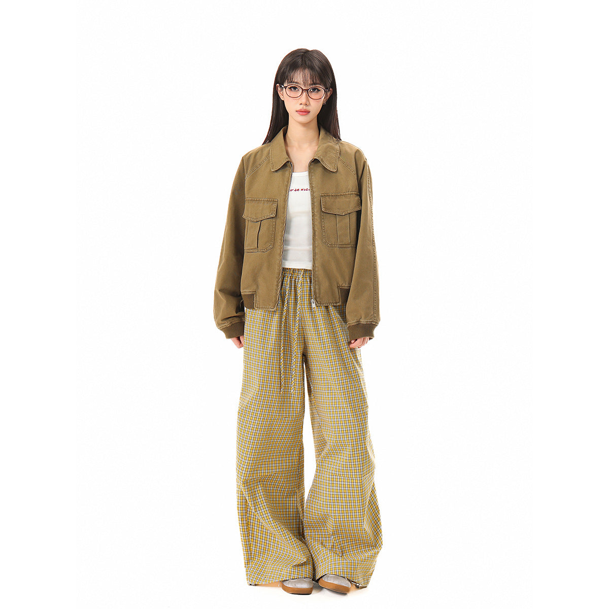 Model wearing an olive-brown jacket with a collar, zip front, and flap pockets, paired with yellow plaid trousers.