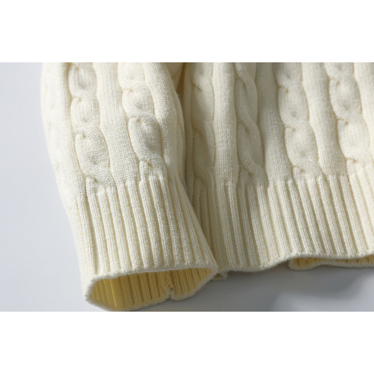 Close-up of an ivory cable-knit sweater showing its ribbed hem and textured body.