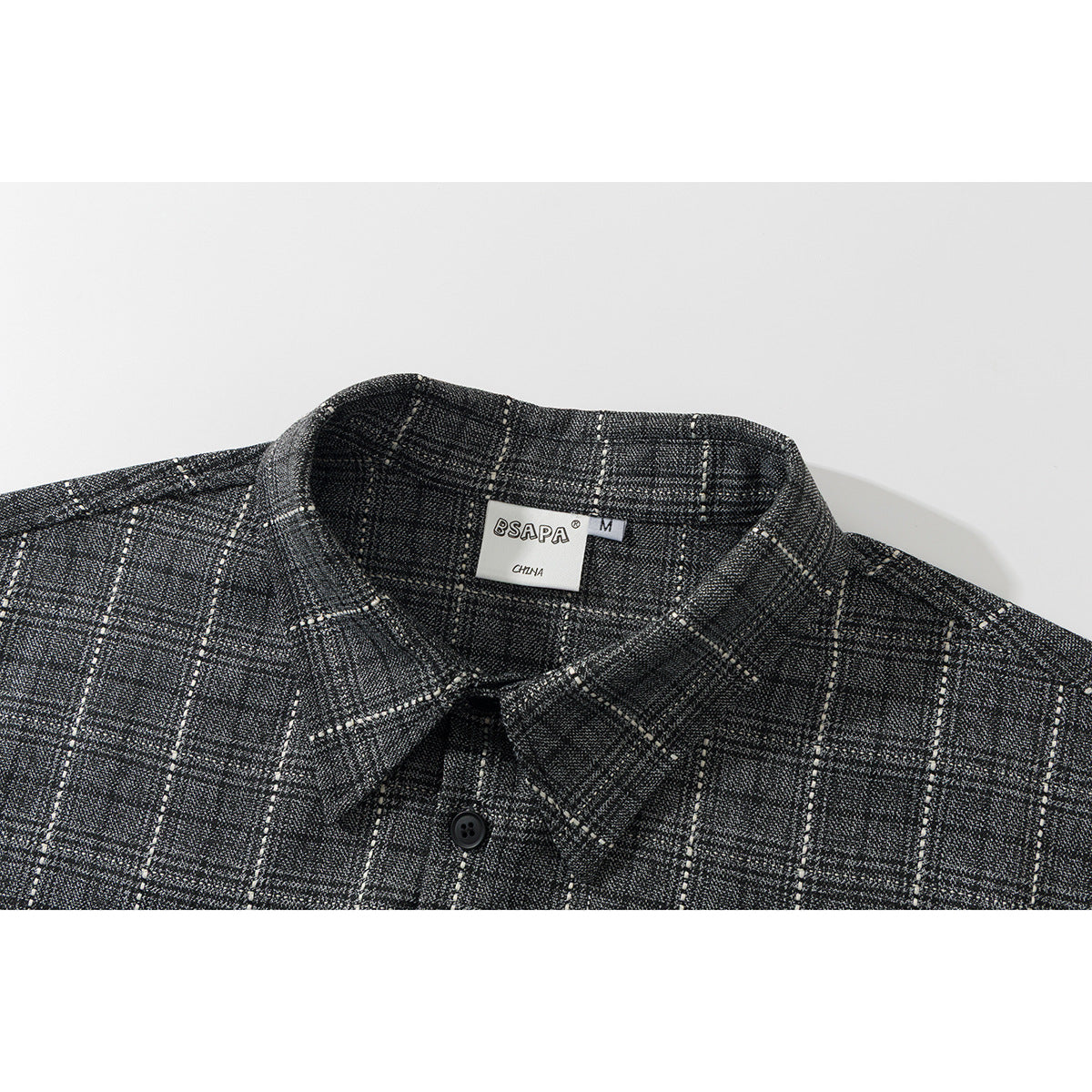 Close-up of a black-and-gray plaid shirt collar, button, and neck label.