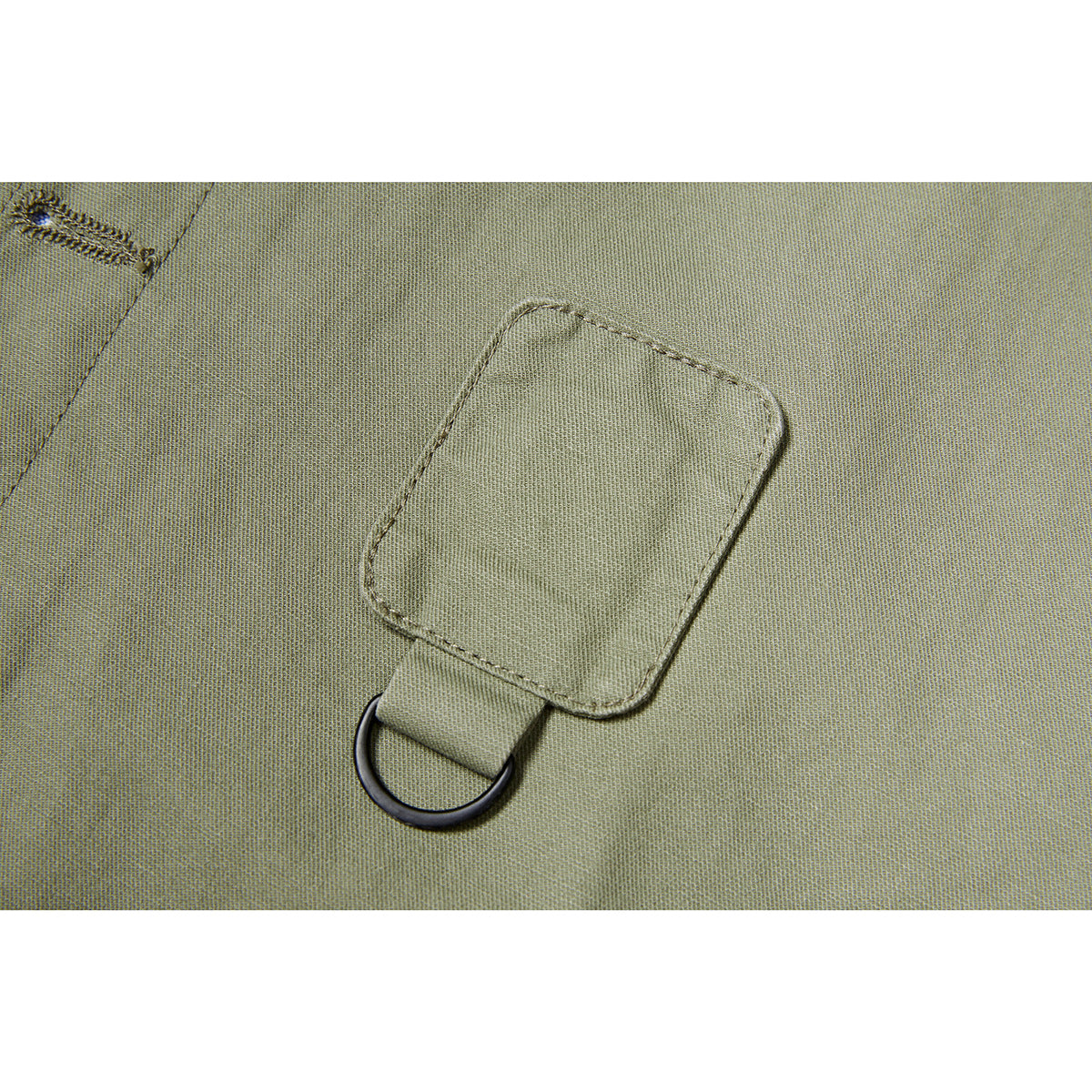 Close-up of an olive jacket’s stitched fabric tab and attached black D-ring.