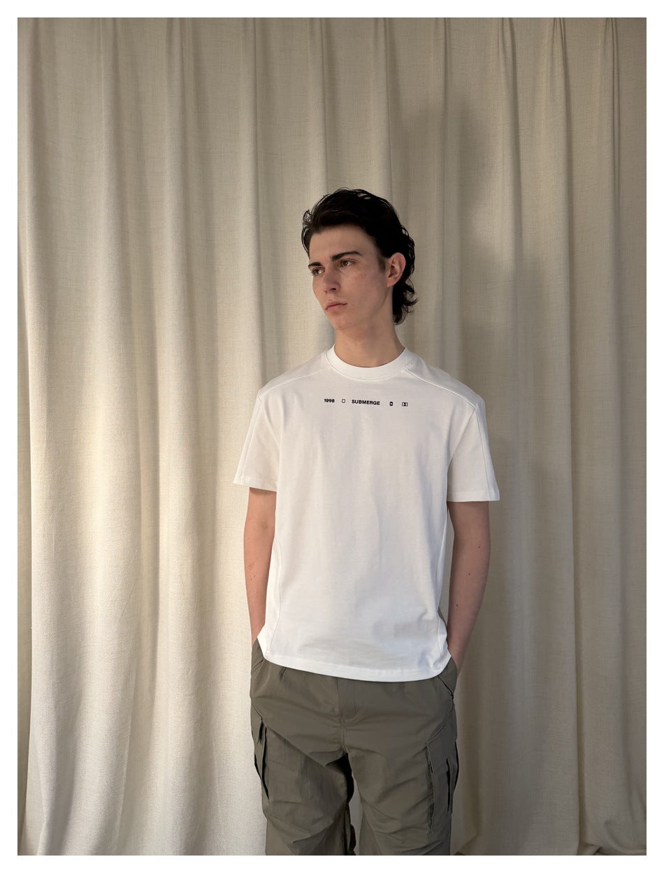 Waist-up front view of a model wearing a white T-shirt with small chest text and gray cargo pants.