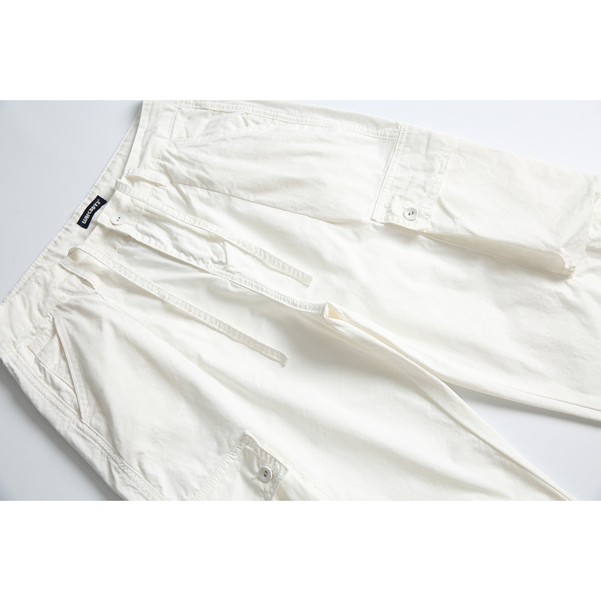 Close-up of off-white cargo pants showing the drawstring waist and buttoned pocket flaps.
