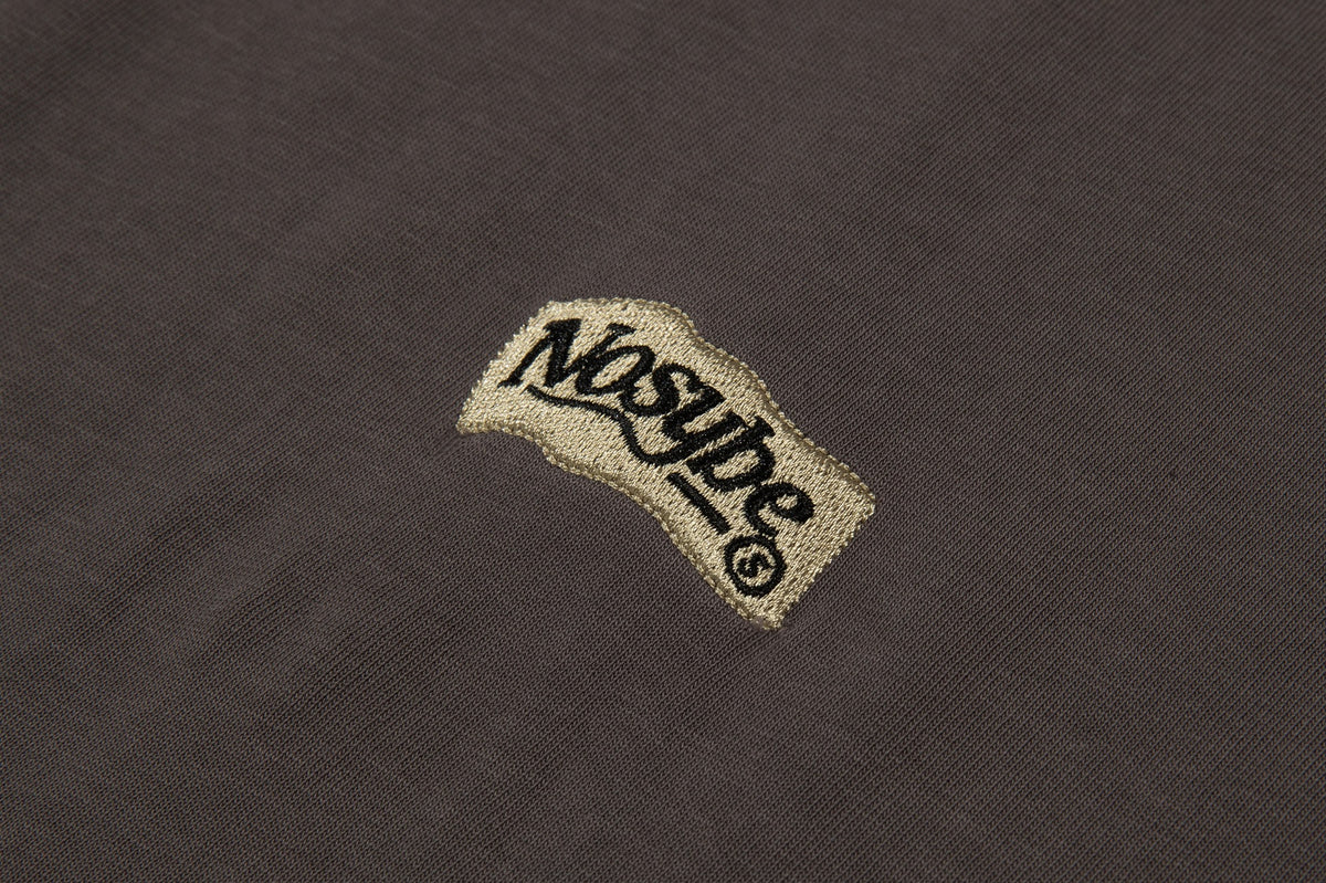 Close-up of a gold embroidered wordmark on dark brown shirt fabric.