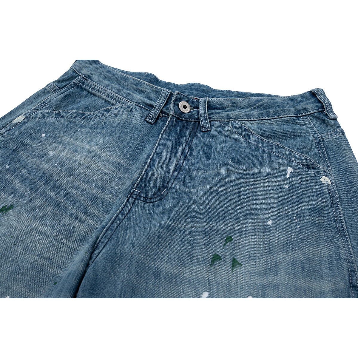 Close-up of blue jeans showing the waistband, front pocket seams, and scattered white and green paint-like marks.