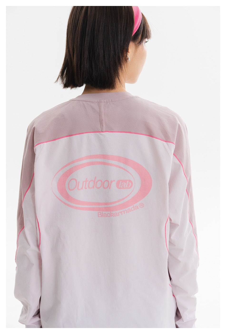 Close rear view of a model wearing a pale pink long-sleeve top with bright pink piping and a large back print.