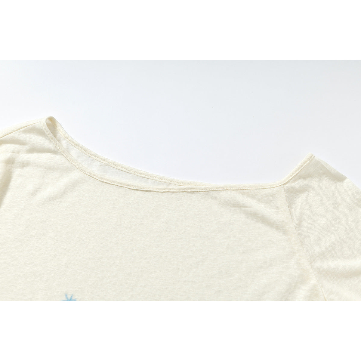 Close-up of the wide neckline and shoulder seam of an ivory long-sleeve shirt.