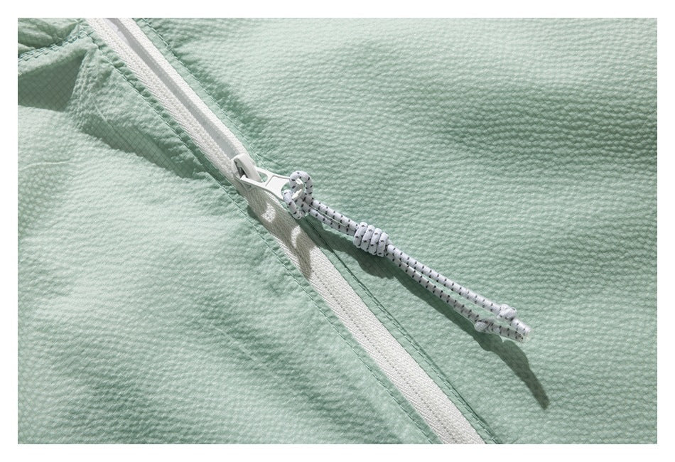 Close-up of a white zipper and speckled cord pull on mint-green textured fabric.