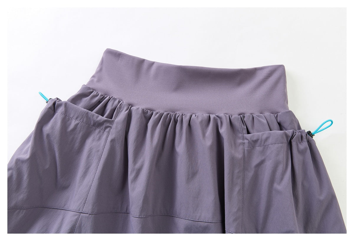 Close-up of a muted purple skirt waistband with gathered fabric, large pockets, and turquoise cord loops.