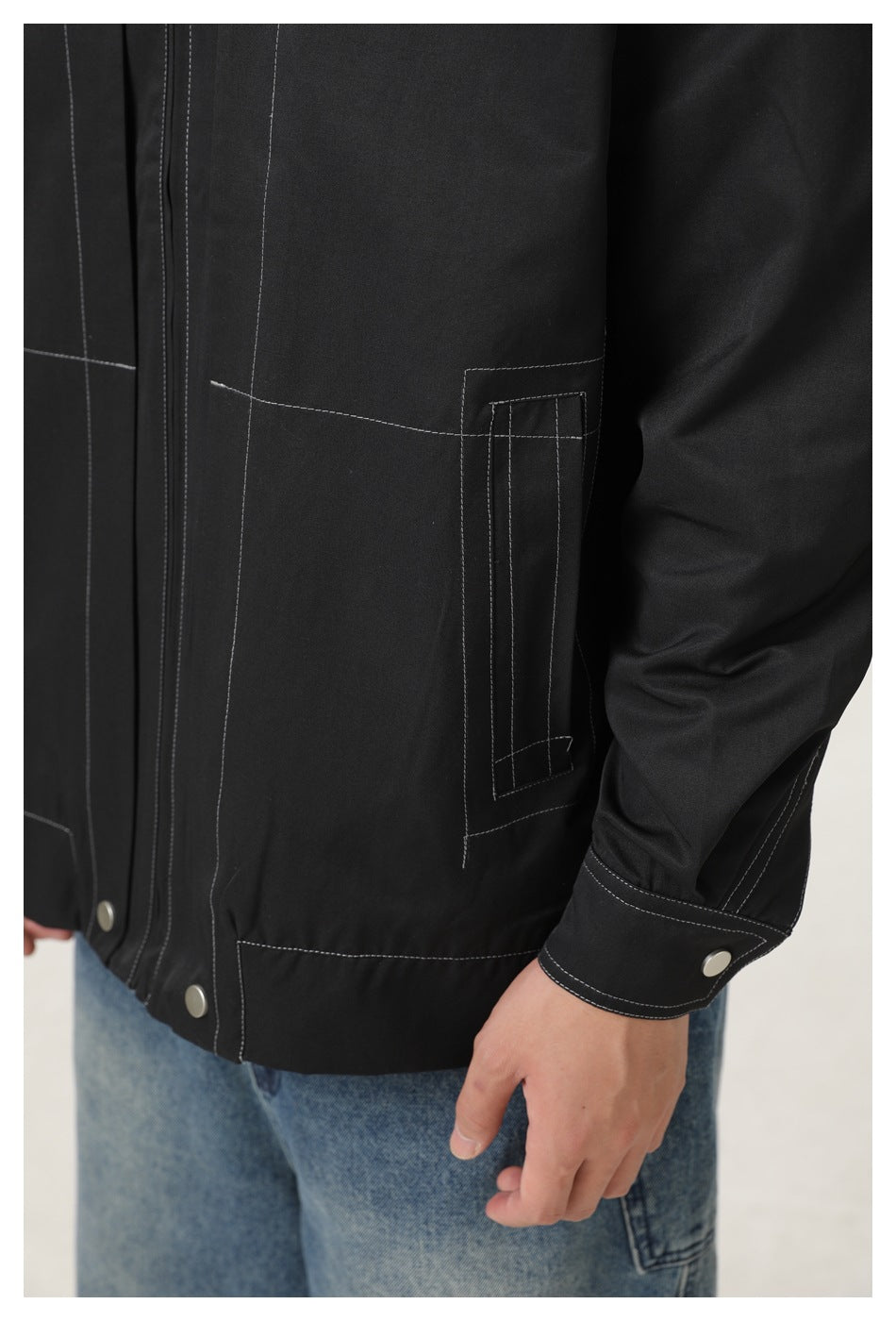 Close-up of the black jacket's lower patch pocket, contrast stitching and snap-button cuff.