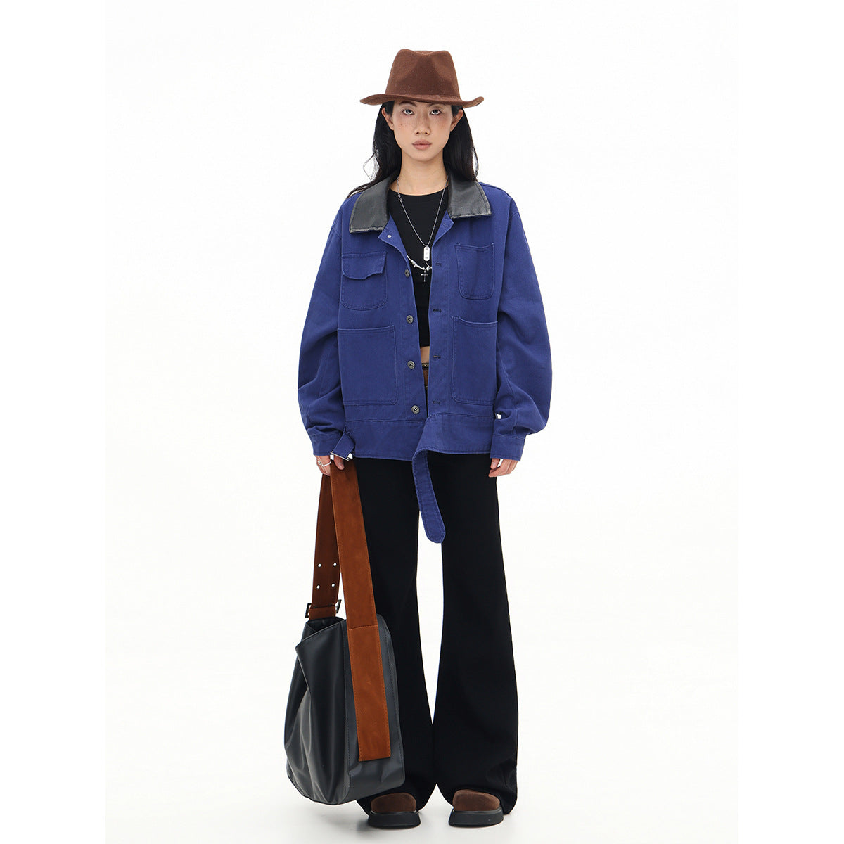Full-length model wearing a cobalt-blue utility jacket with a black collar and long belt, styled with black flared trousers