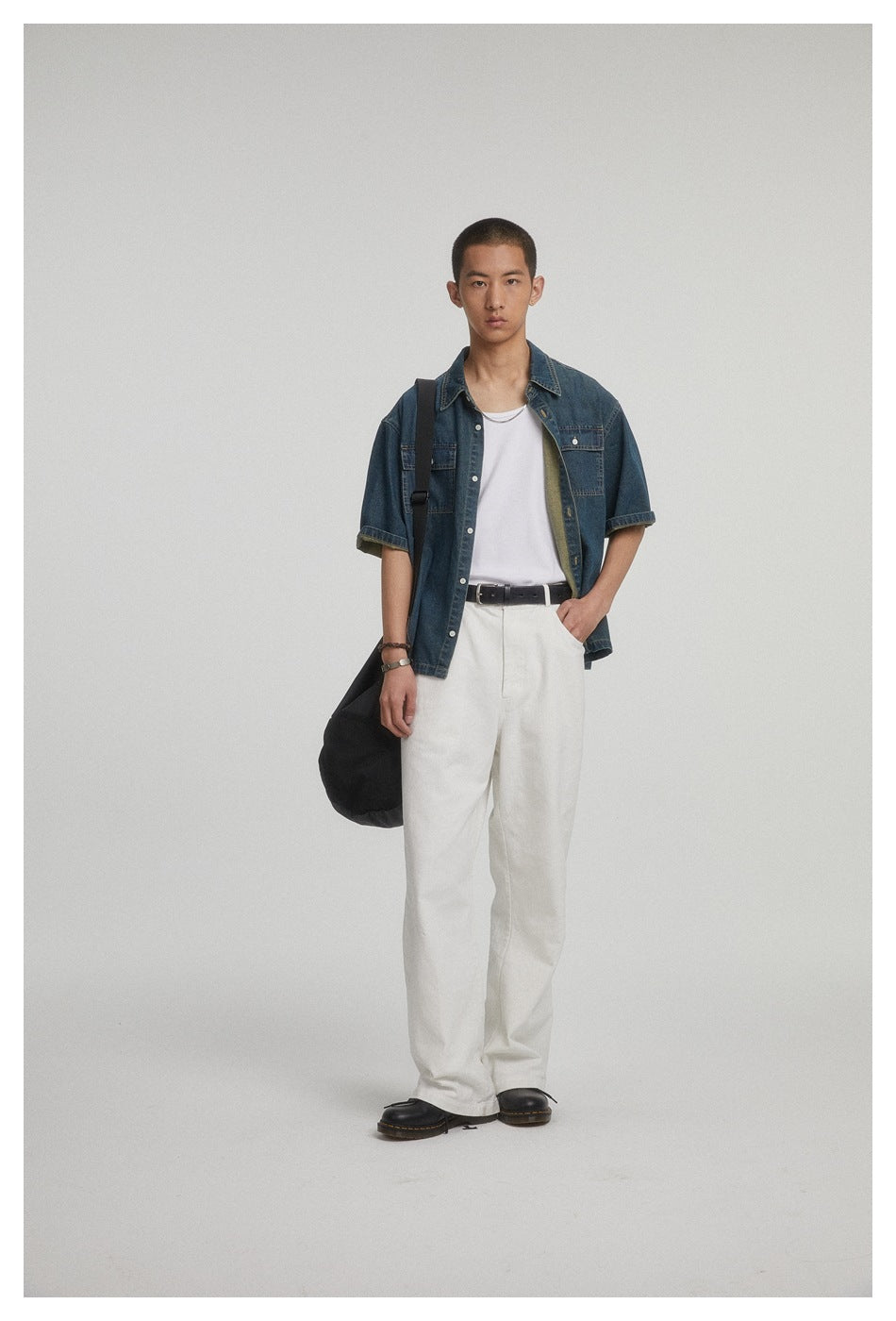 Front-facing model wearing an open dark blue short-sleeve denim shirt over a white tee with loose white trousers.