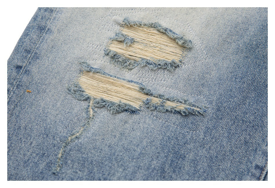 Close-up of two frayed horizontal rips with exposed threads in light-wash blue denim.