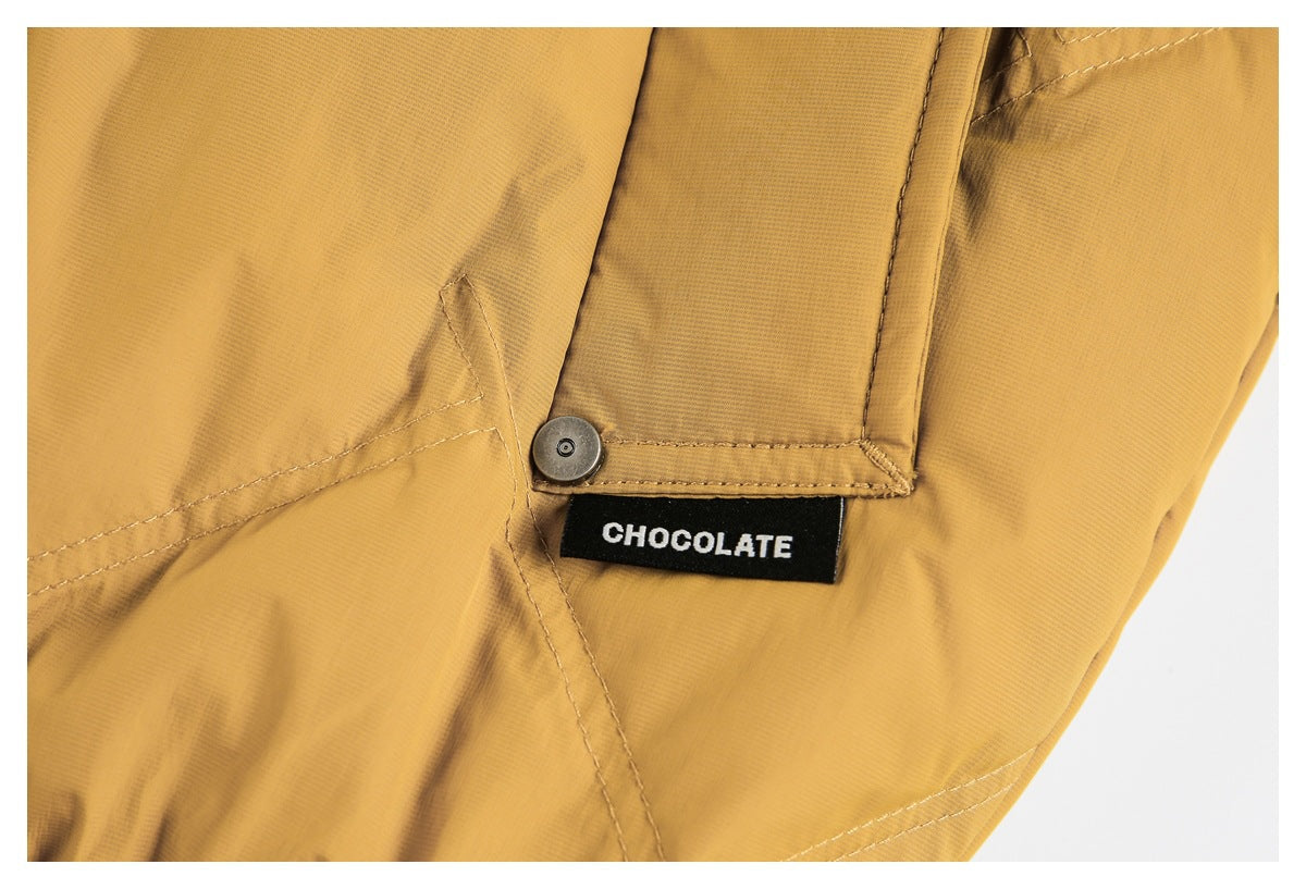 Close-up of a mustard-yellow jacket seam and snap fastener beside a black sewn-in label reading “CHOCOLATE.”