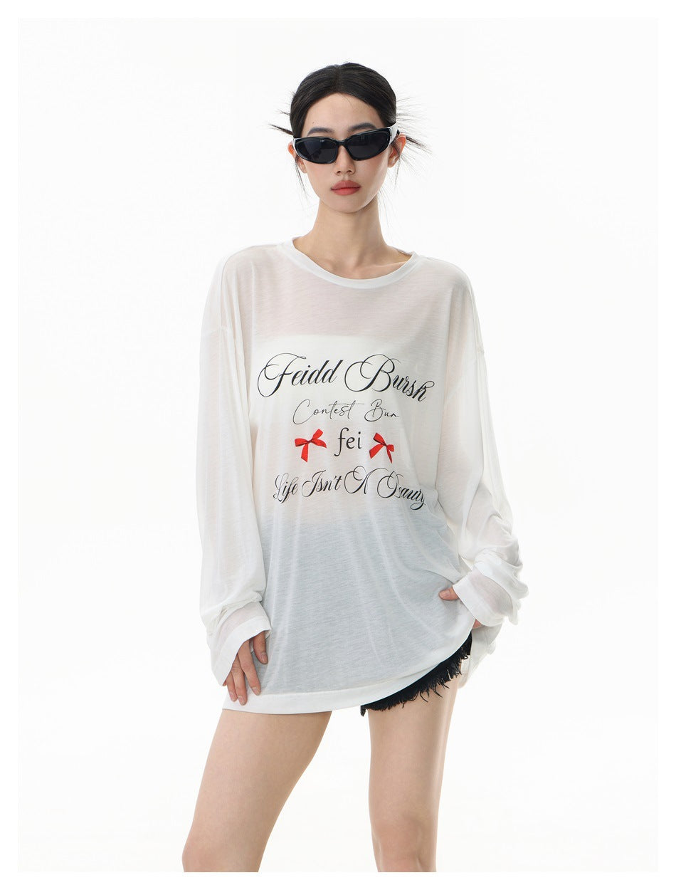 Front view of a model wearing an oversized sheer white long-sleeve tee with black script and red bow graphics.