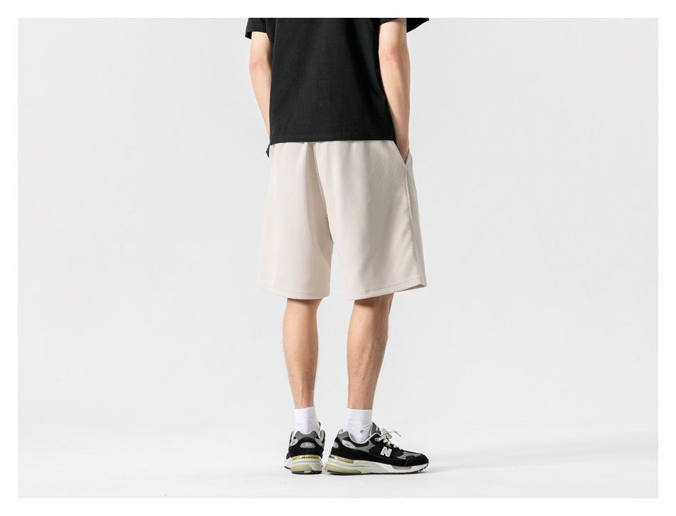 Rear view of a model wearing plain light beige knee-length shorts.