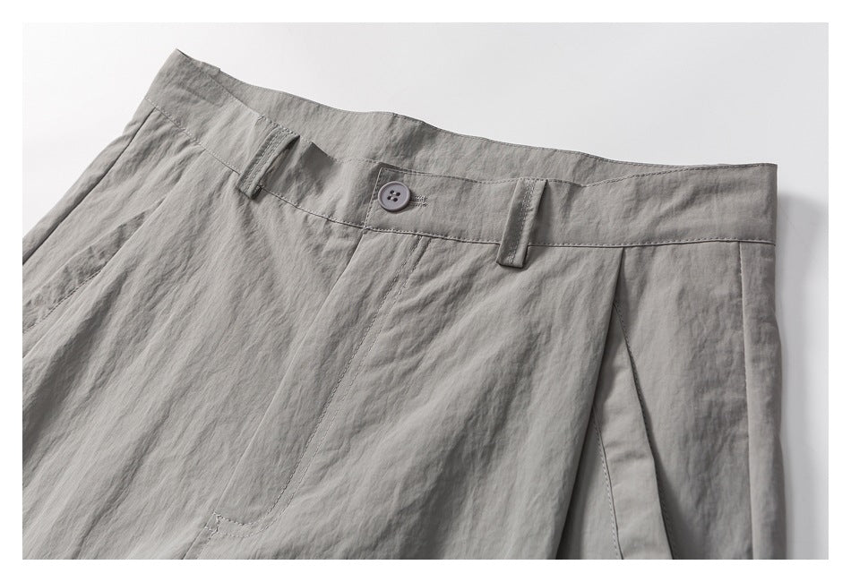 Close-up of the gray shorts' front waistband, button, belt loops, and pocket stitching.