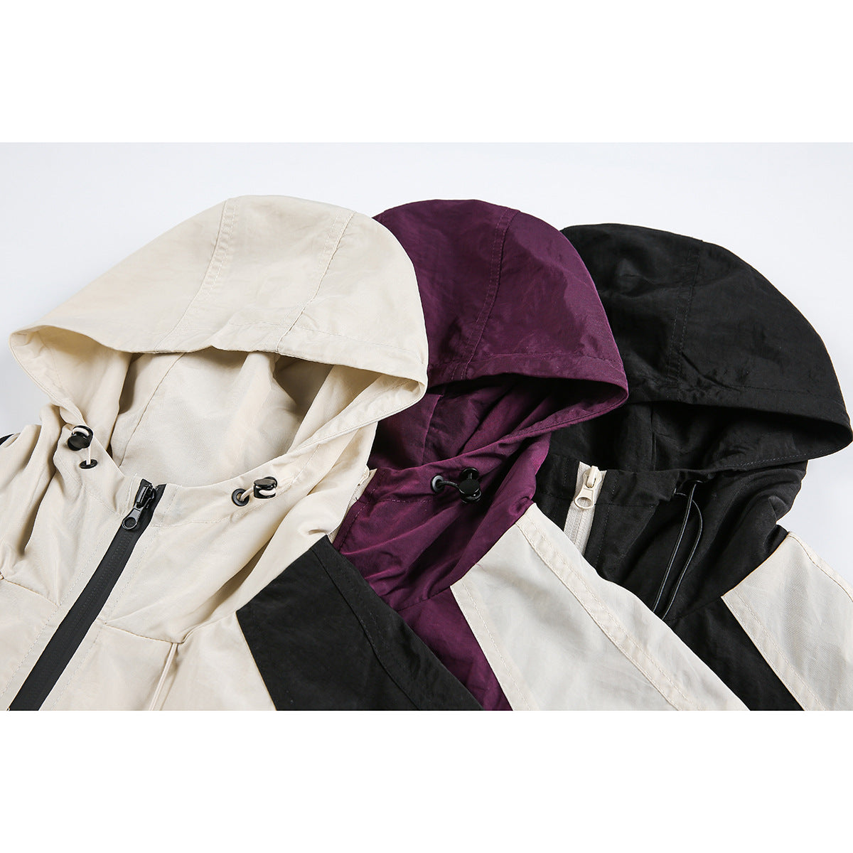 Close-up of cream, plum, and black hooded vests showing the hoods, drawcords, and front zippers.