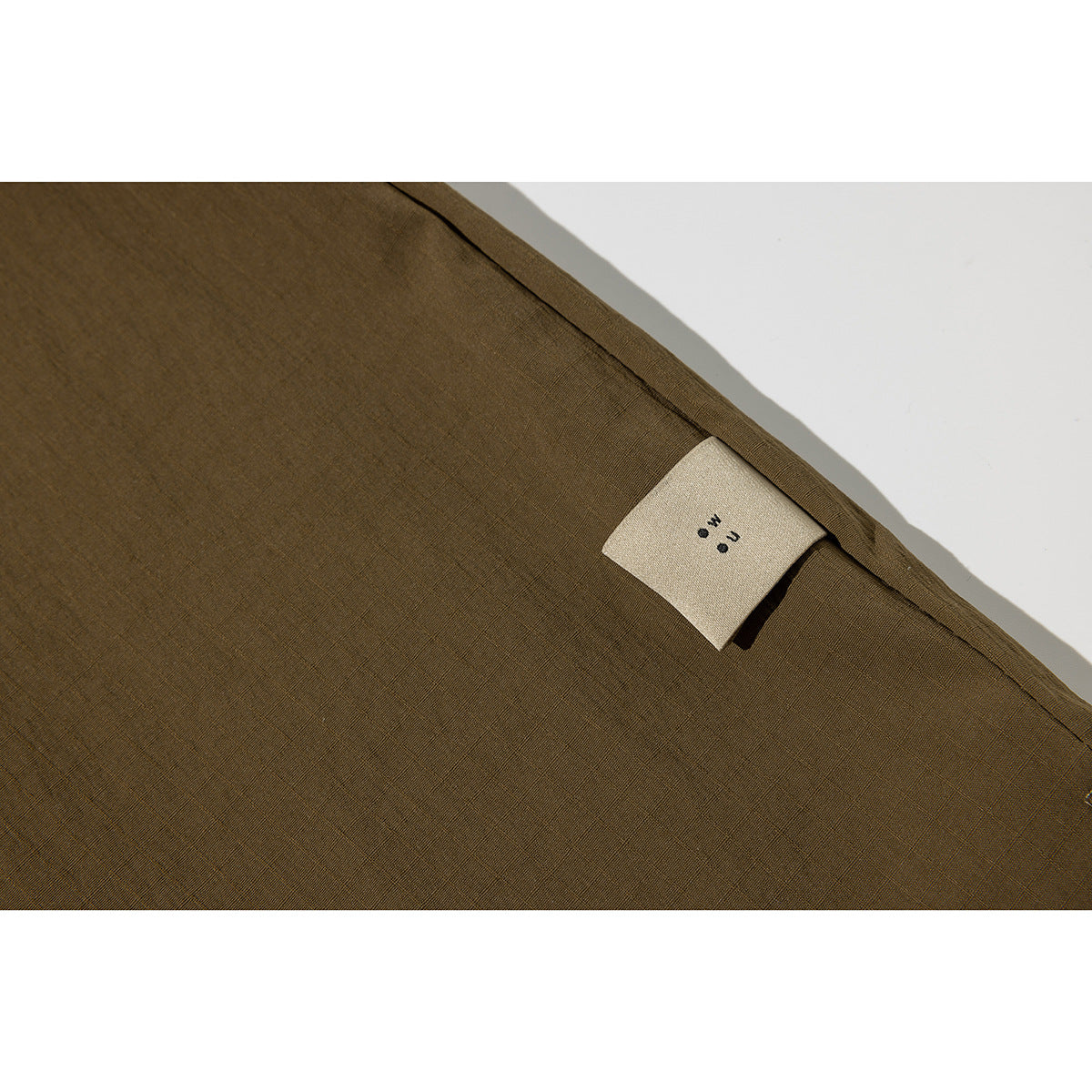 Close-up of olive-brown shirt fabric and a small sewn-in label near a seam.
