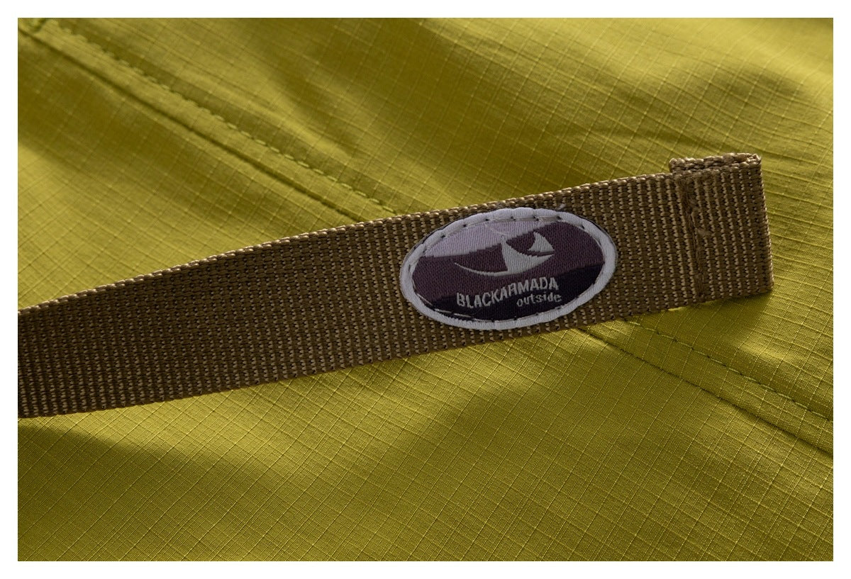 Close-up of a brown webbing belt with an embroidered oval brand patch against olive-yellow fabric.