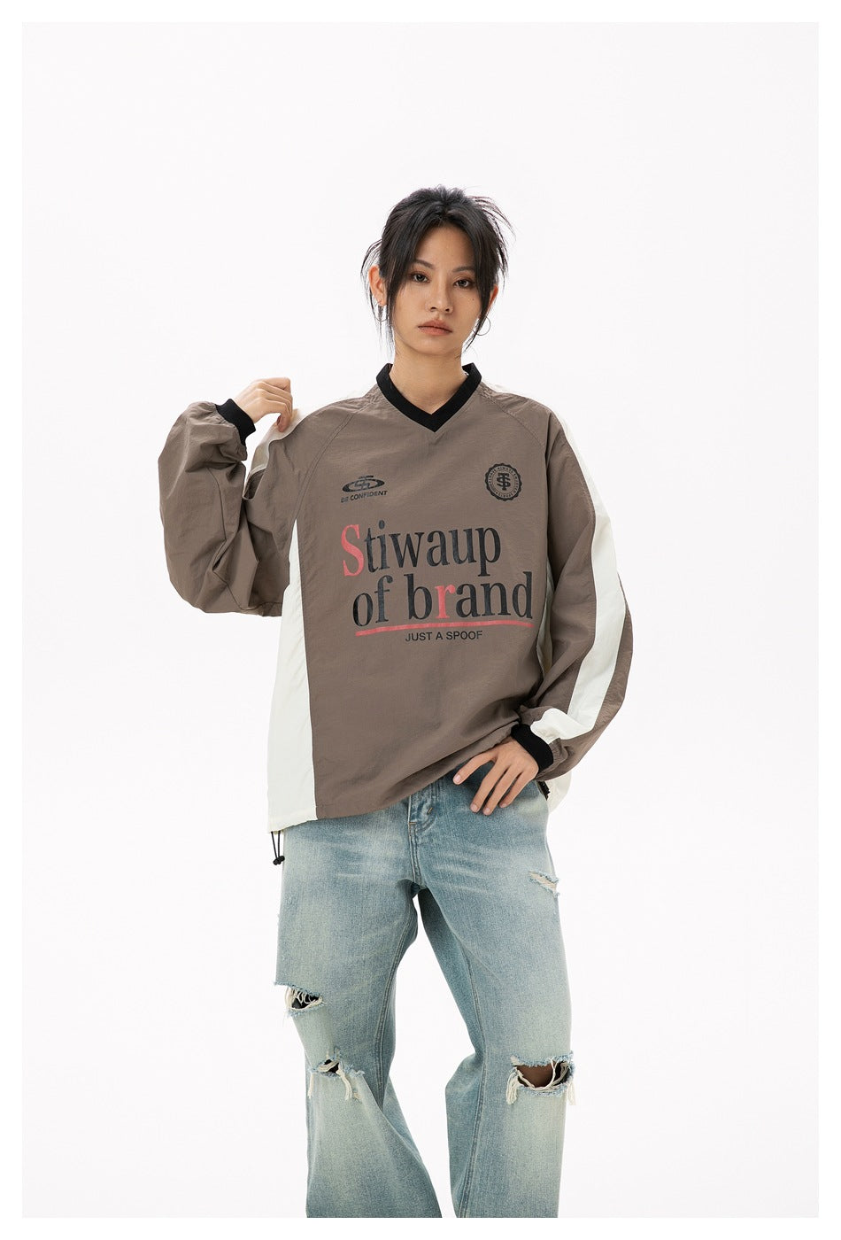 Model wearing a taupe V-neck pullover with cream side panels, black trim and large front lettering.