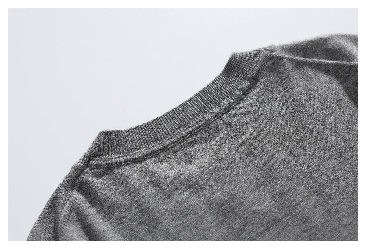 Close-up of a gray knit sweater showing its ribbed crew neckline and shoulder seam.