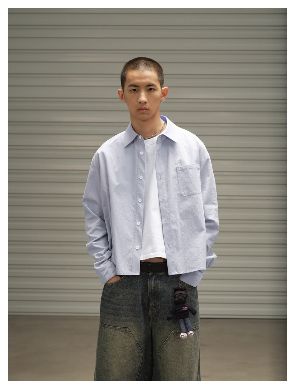 Waist-up front view of a model wearing a pale blue button-up shirt over a white tee; the shirt has a single chest pocket.