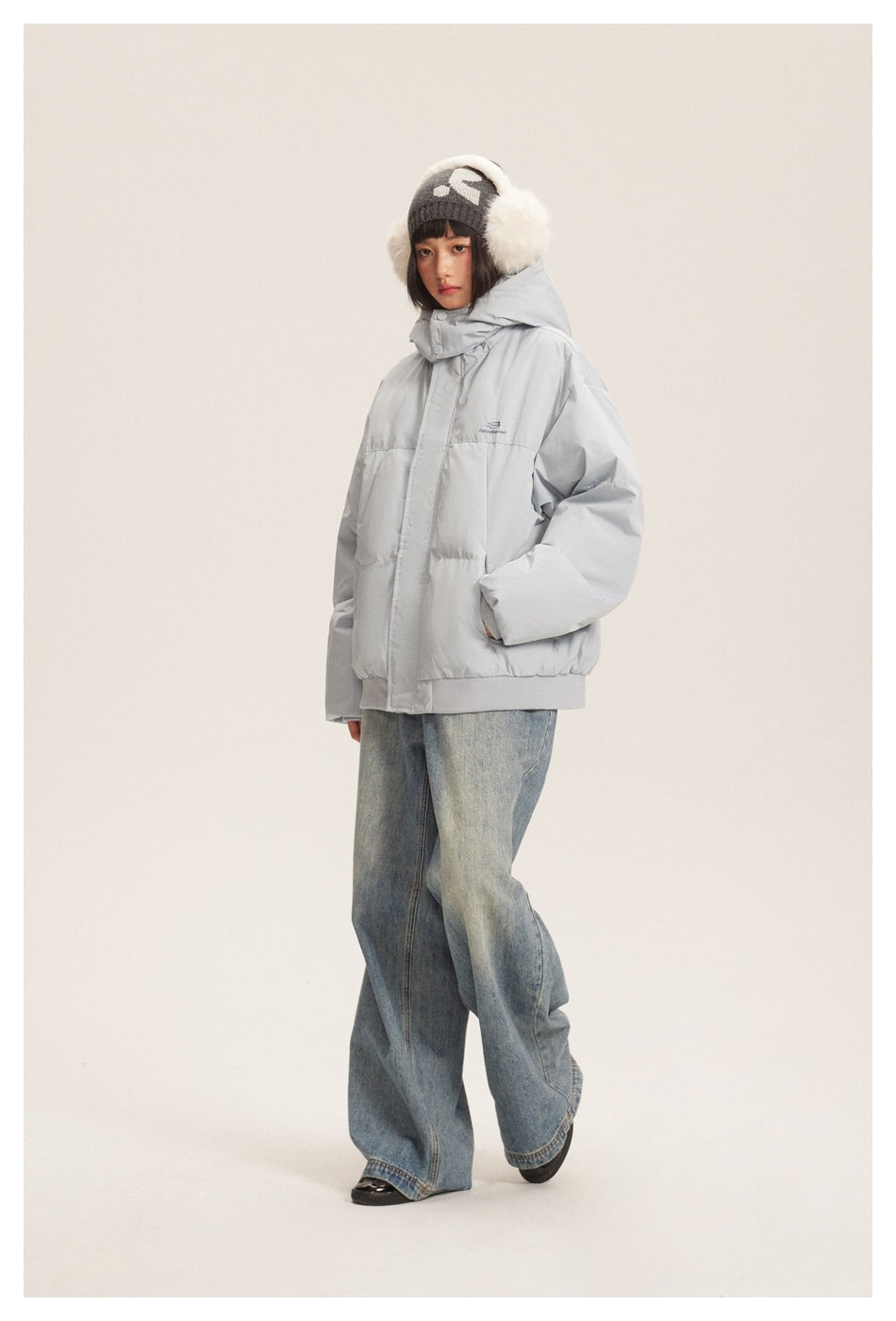 Full-length angled view of a model wearing a light gray hooded puffer jacket and wide-leg jeans.