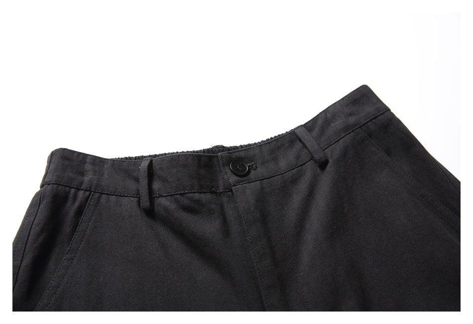 Close-up of the front waistband of black shorts, showing the button, belt loops, and angled pocket seam.