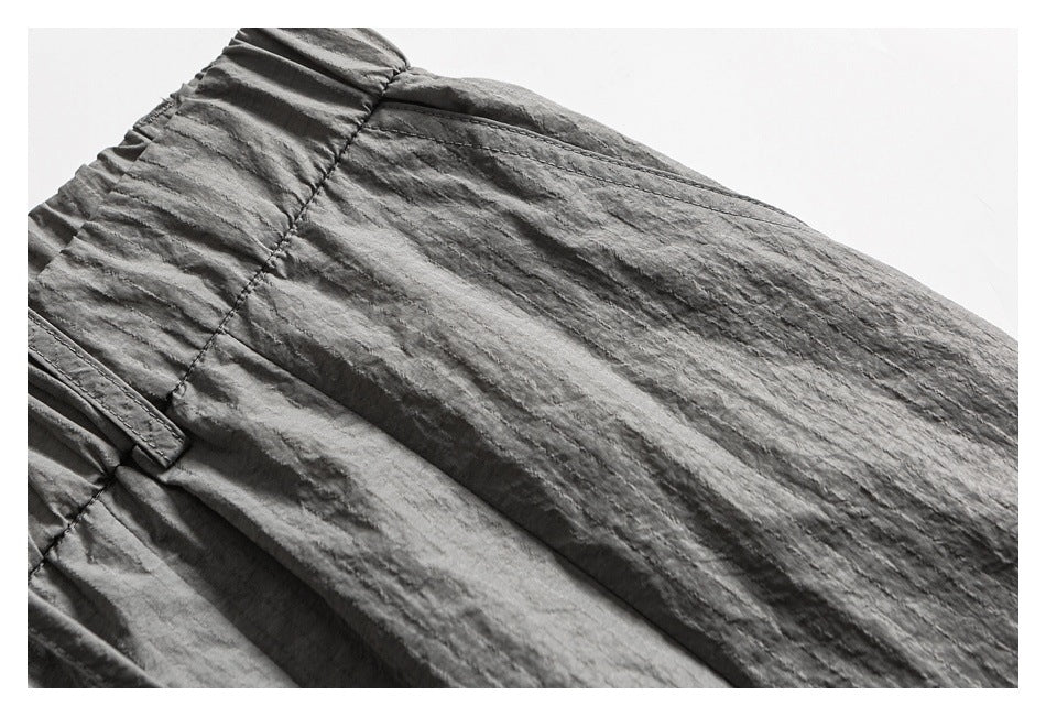 Close-up of gray cargo pants showing the gathered waistband, belt loop, seams, and crinkled surface texture.