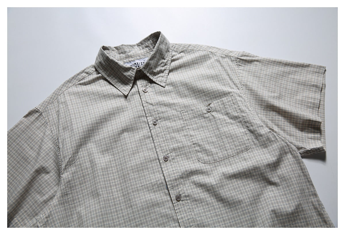 Flat-lay front view of a light gray plaid short-sleeve button-up shirt with a single chest pocket.