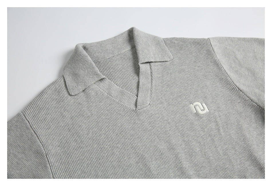 Partial front view of a light gray rib-knit sweater with a folded collar and small white chest emblem.