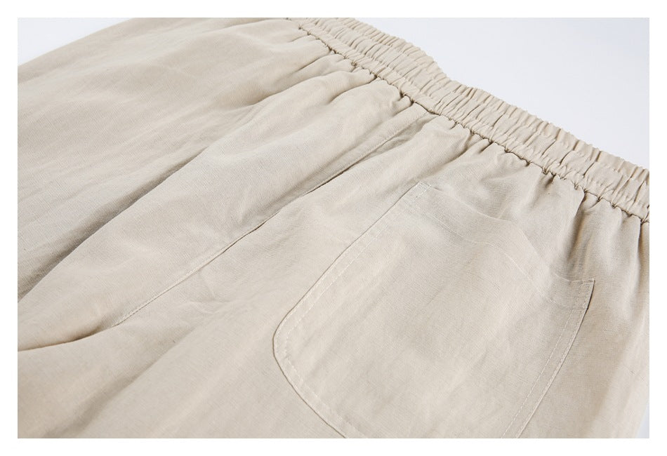 Angled close-up of beige trousers showing the gathered elastic waistband and back patch pocket.