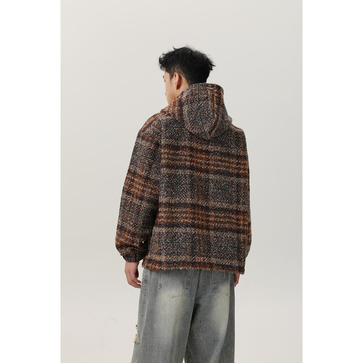 Rear view of a man wearing a brown, charcoal and beige striped hooded pullover with loose gray jeans.
