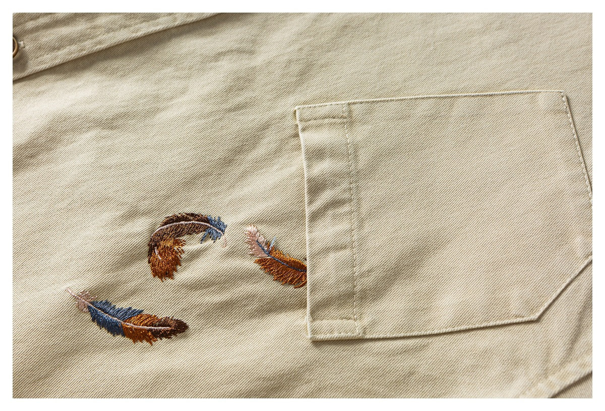 Close-up of a beige twill jacket with a large chest pocket and three multicolored feather embroideries.