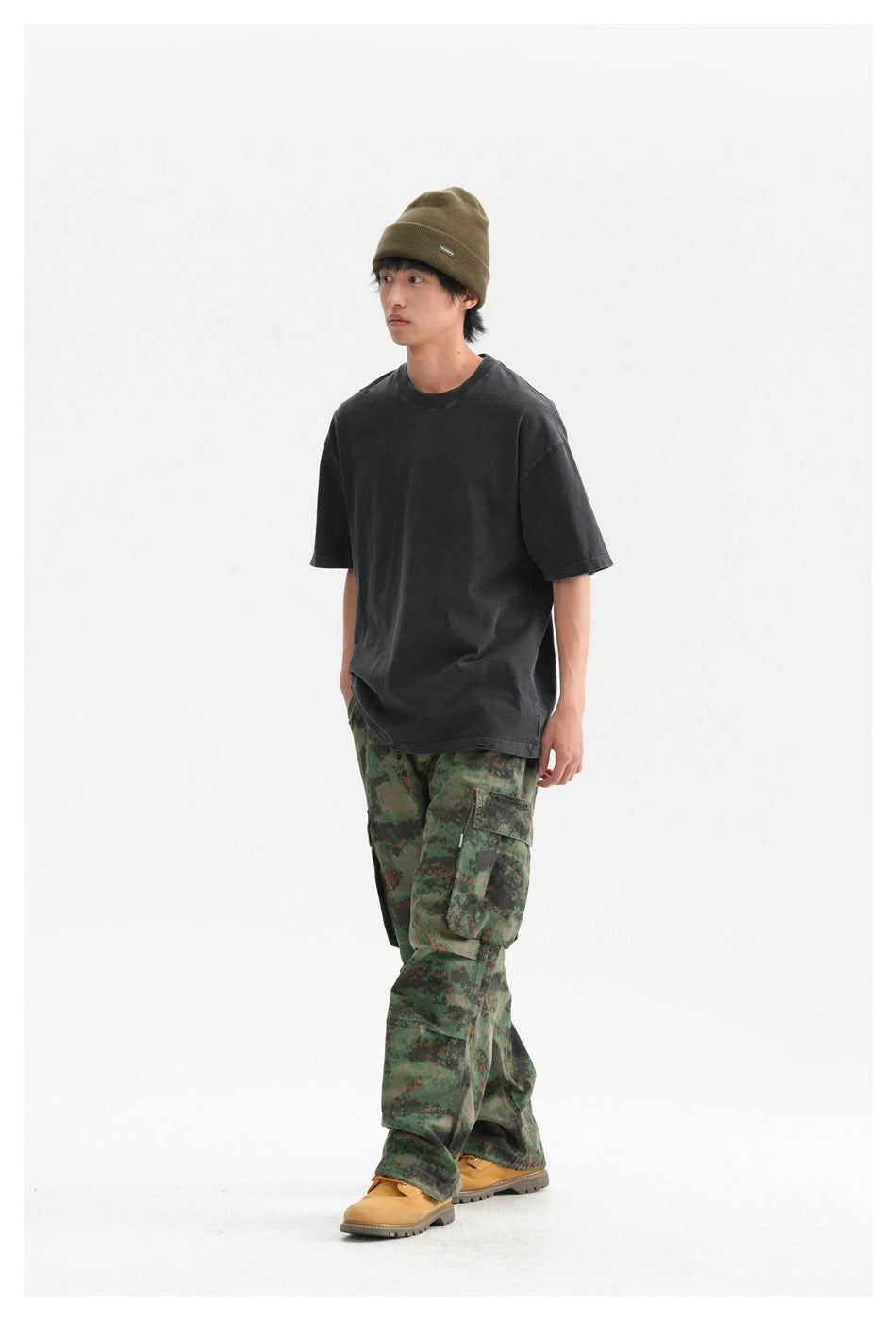 Full-length model wearing an oversized charcoal T-shirt, green camouflage cargo pants, and an olive beanie.