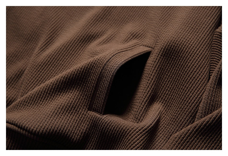 Close-up of an angled pocket opening on the brown hoodie, showing its ribbed texture and stitching.
