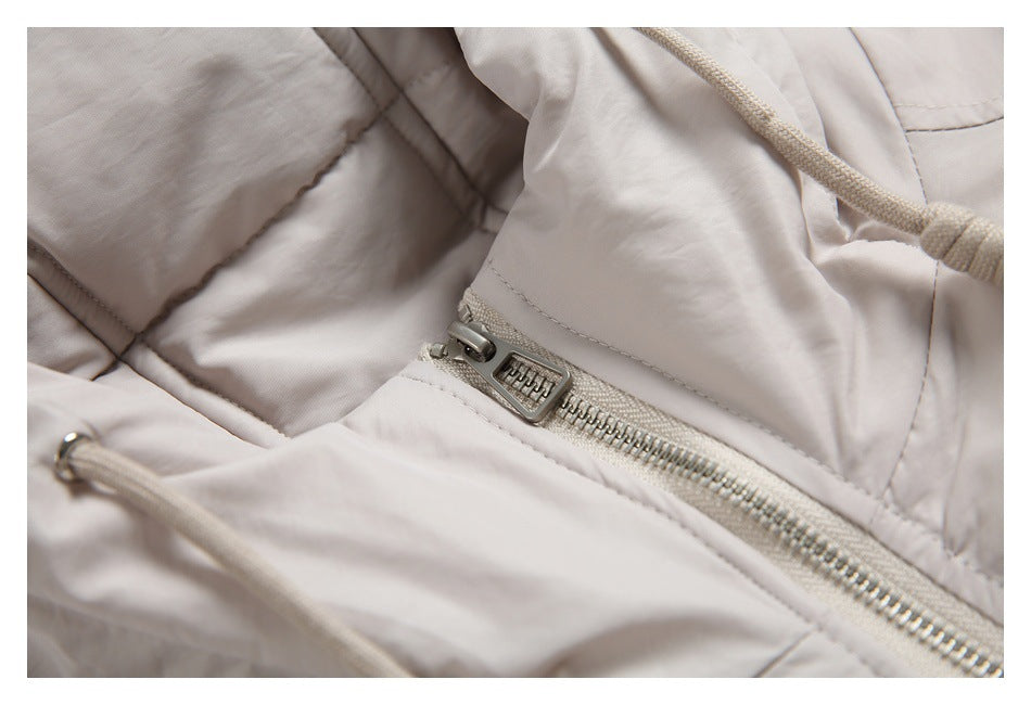 Close-up of a light beige jacket's padded fabric, front zipper, and drawcord.