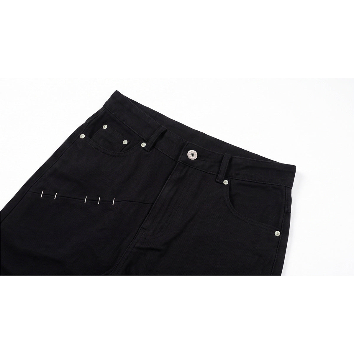 Close-up of black jeans showing the waistband, front pockets, metal rivets, and contrasting stitch details.