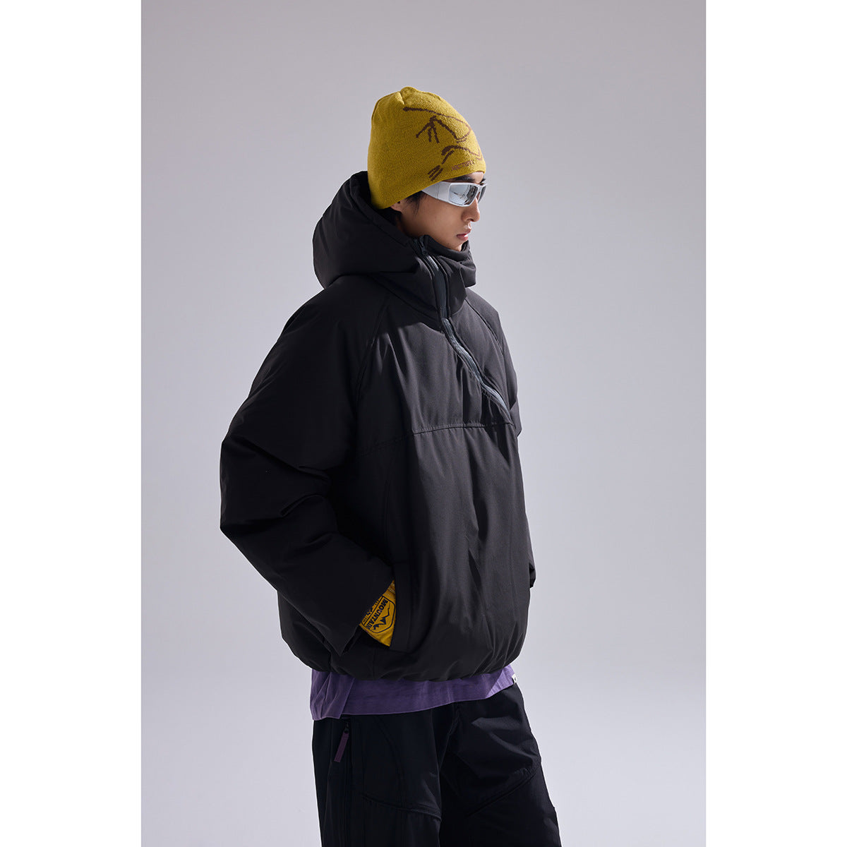 Side view of a model wearing a black hooded jacket, black pants, and a yellow beanie.