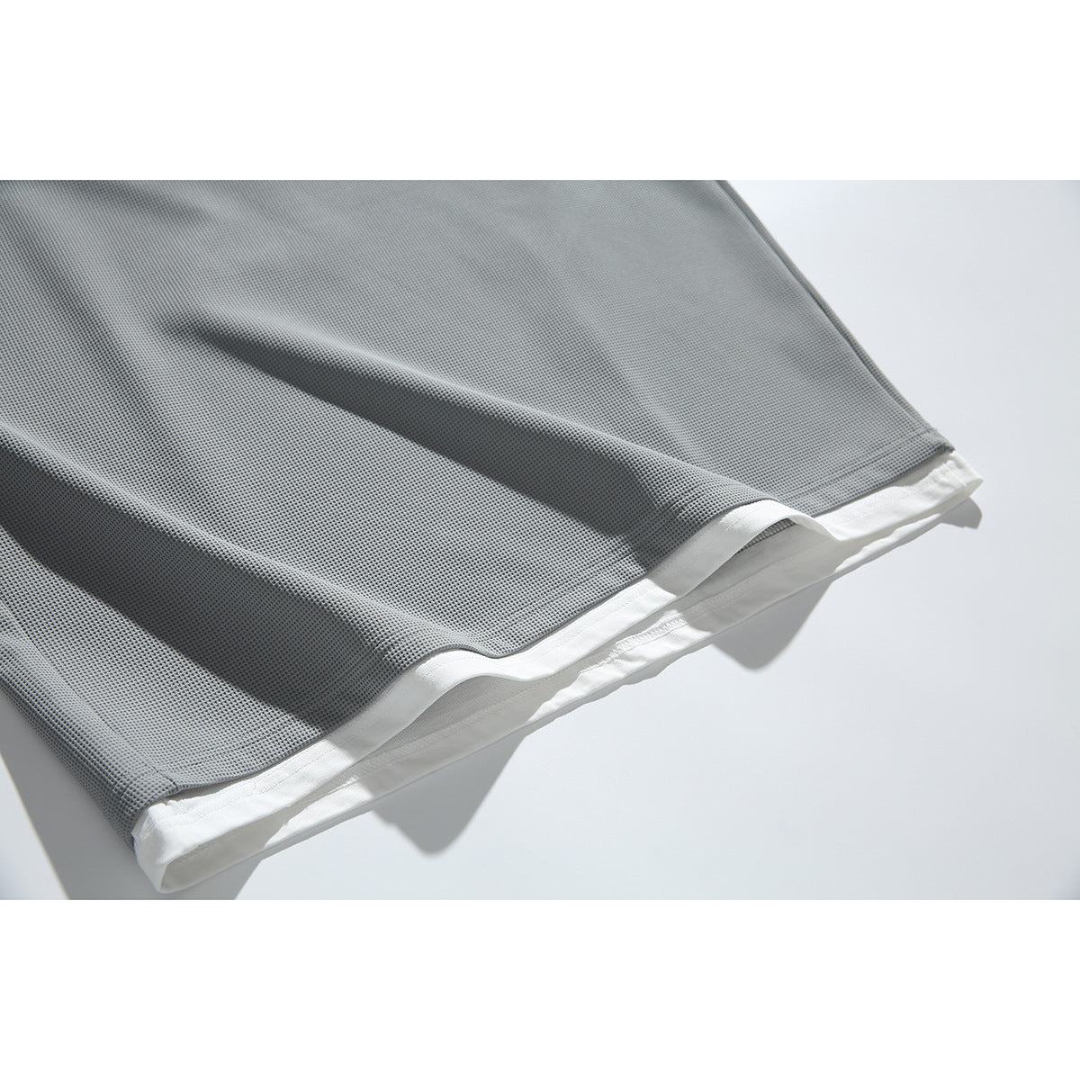 Close-up of a gray textured top's hem with a white layer showing beneath it.