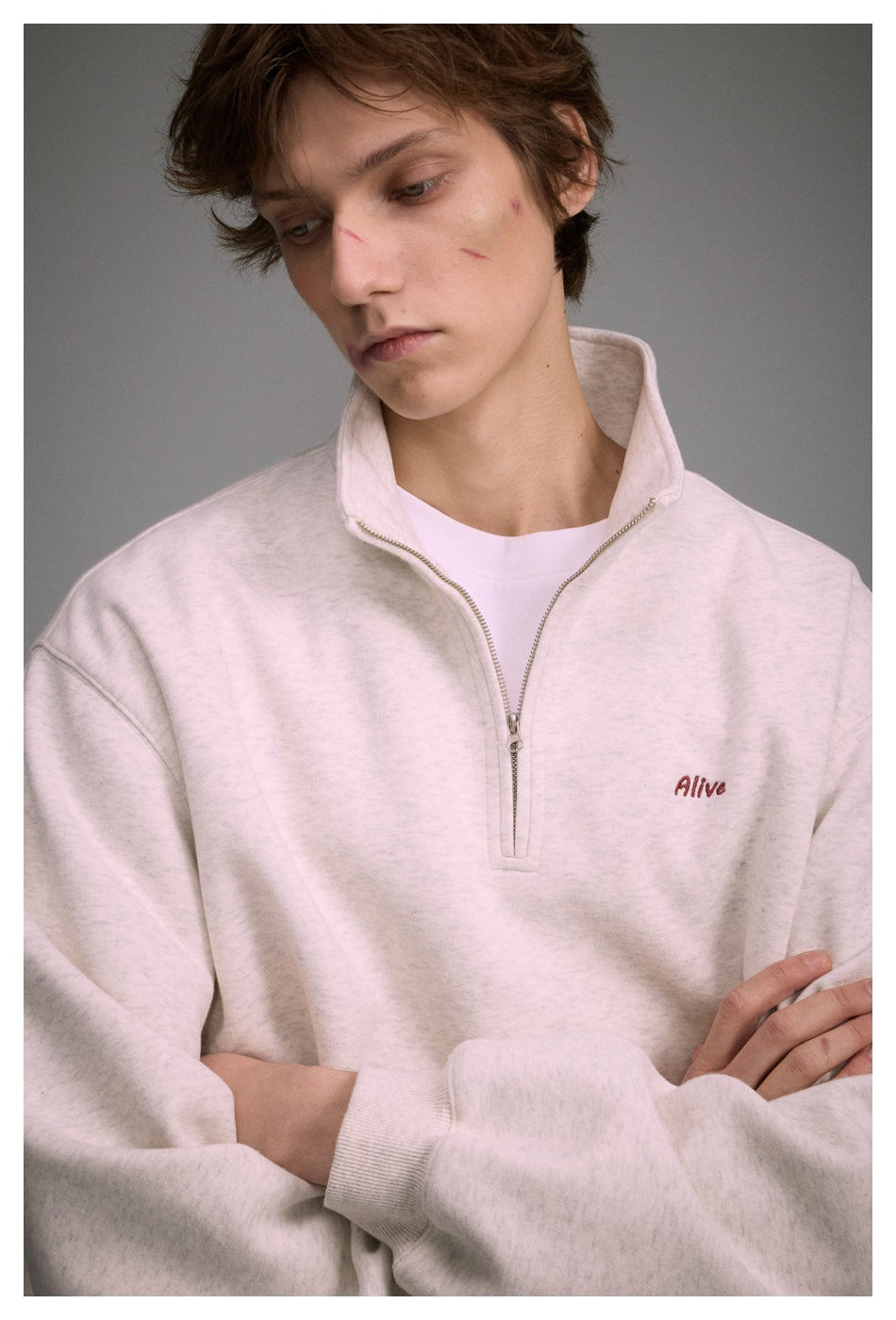 Close view of a model wearing a light heather sweatshirt with a raised collar, silver quarter zipper, and small chest