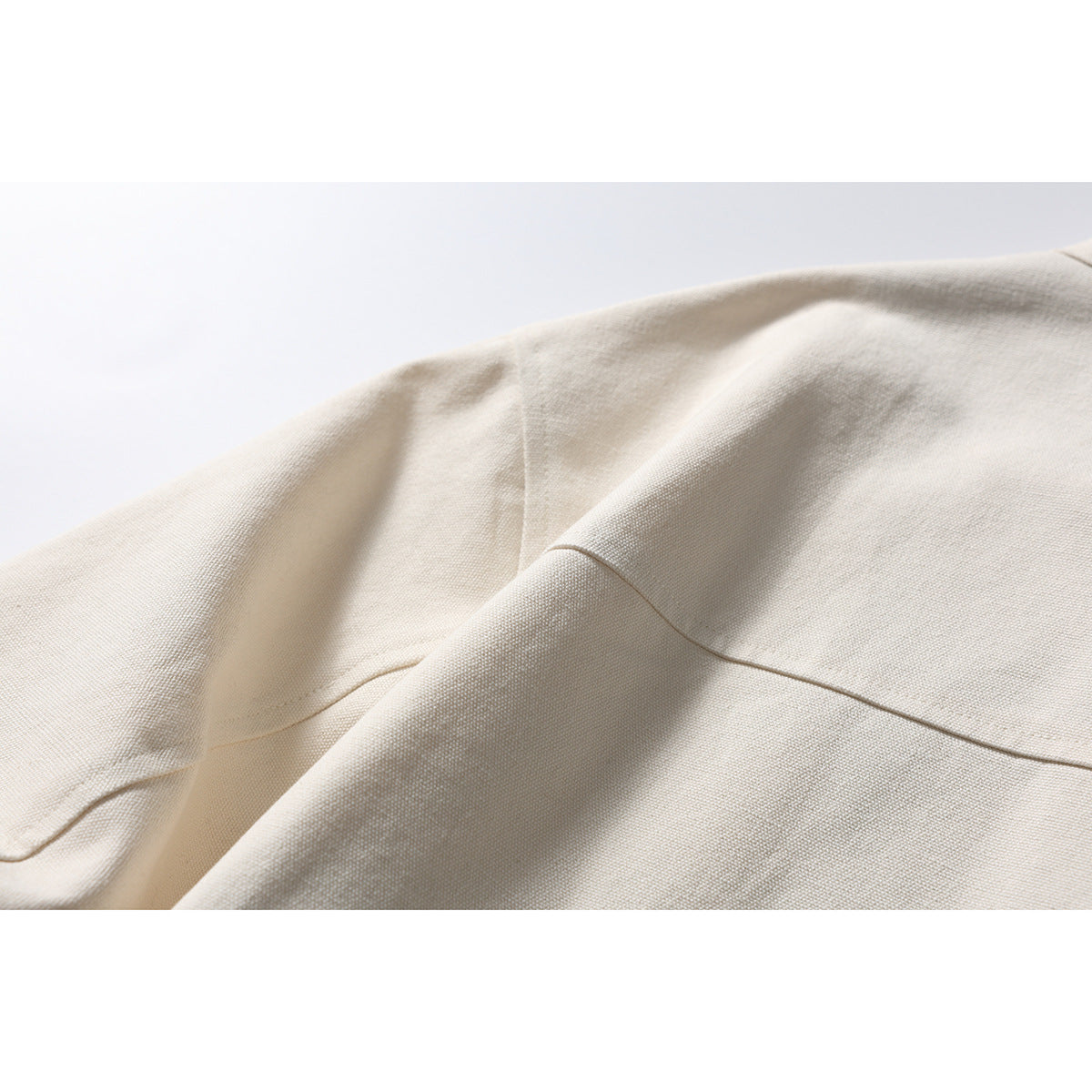 Close-up of the ivory jacket's woven-looking surface, folded fabric, and stitched seam.